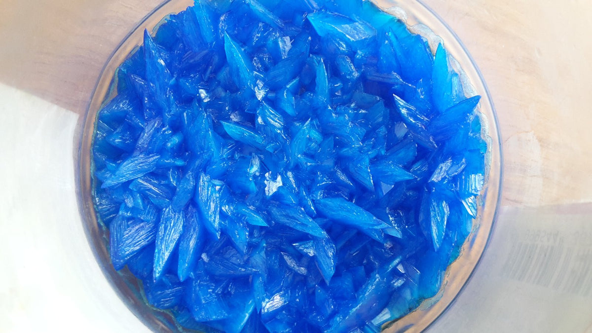 Bright blue copper sulfate crystals in a glass dish